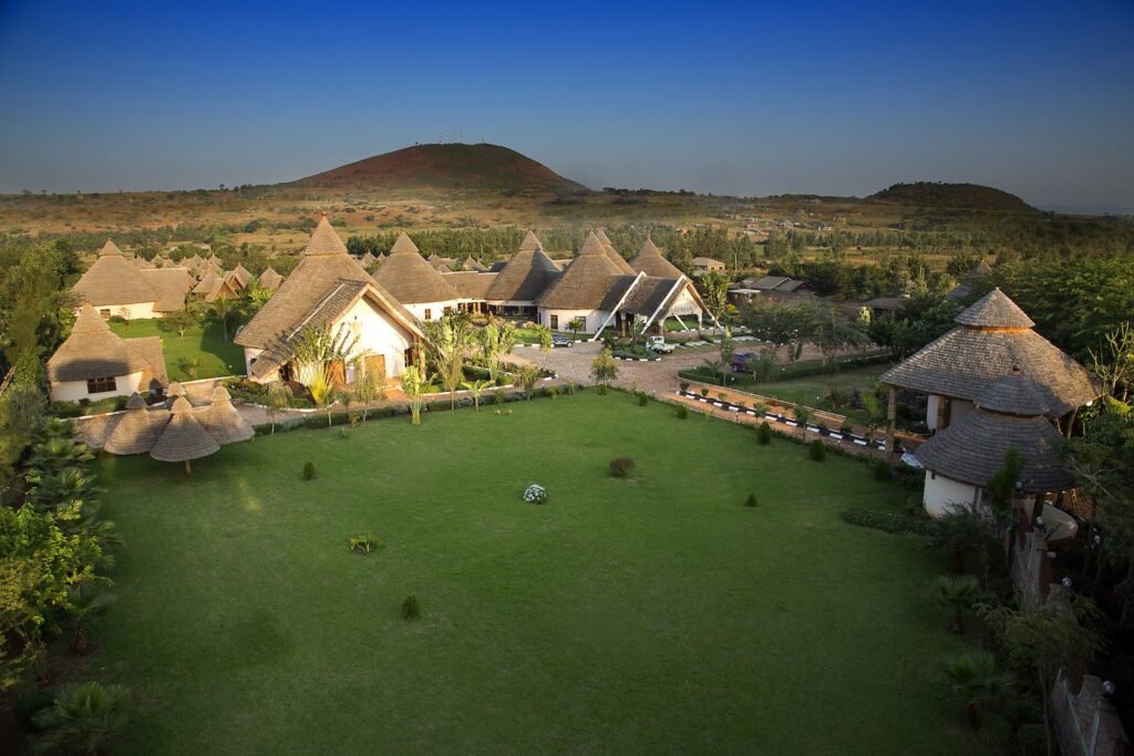 An elevated view over the thatched guest houses and lawns, with hills beyond, at Farm of Dreams Lodge, Karatu