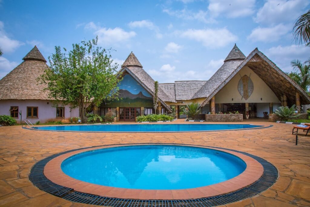 The swimming pool with thatched buildings behind on a clear day at Farm of Dreams Lodge, Karatu